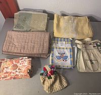 Overview of assorted kitchen linens including Thanksgiving-themed napkins, aprons, placemats, tea cosy