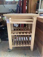 Full view of the solid wood kitchen cart showing the drawer pulled out, two open slatted shelves, and caster wheels.