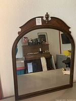 Front view of the full large wooden framed mirror reflecting a piano and surrounding room.