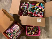 Box filled with partially assembled Lego Friends buildings and yacht pieces, including pink, purple, and teal colored blocks.