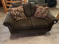 Front view of the brown upholstered loveseat showing two seat cushions and two decorative patterned pillows.