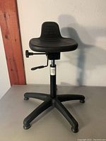 Front view of black office stool showing molded seat, backrest, levers, and five-legged base.
