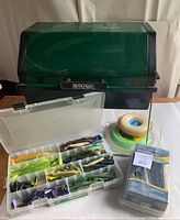 Plastic tackle box with a variety of soft and hard fishing lures in different colors, plus coil of dock line and packaged weed trimmer line