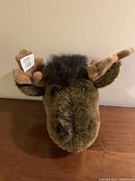 Front view of plush moose head showing soft brown fur, cream antlers, ears, and detailed facial features.