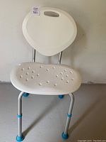 Front view of a white plastic shower seat with a contoured seat and backrest, supported by metal legs with blue foot grips.