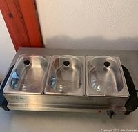 Three container stainless steel serving tray with clear lids and temperature dial, can convert into a rectangular hot plate. Black plastic handles and knobs visible.