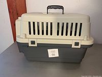 Front side view of beige plastic top and dark gray plastic bottom pet carrier with handle and ventilation slots.