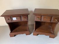 Front view of two wooden bedside tables showing drawers and open shelves