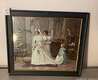 Framed Victorian bride picture showing a bride in white gown with attendants in period dress inside a black frame with some damage.