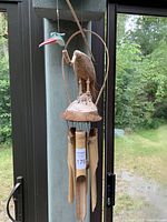 Wooden eagle wind chime hanging by a window with outdoor greenery visible