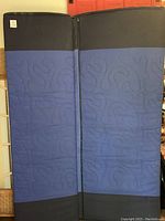 Blue and black mattress standing vertically, showing the fold line where it splits