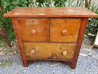 Front view of antique chest showing two small top drawers and one large bottom drawer with wooden knobs and keyholes.