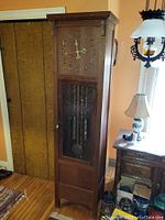 Full view of oak long case clock standing next to furniture and lamp