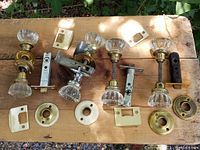 Overhead shot of all four glass doorknob sets with latch mechanisms, rosettes, and faceplates displayed on wooden surface.