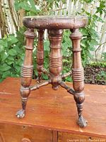 Side angle showing turned spindle legs and carved ball and claw feet of the wooden stool.