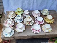 Full view of all 14 cups and saucers arranged on wooden surface