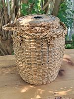 Front and side view showing woven pattern, lid, braided handle, and open hole in lid center.