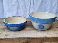 Pair of ceramic kitchenware bowls with blue decorations; larger bowl has metal loops for hanging, smaller bowl shows hairline cracks.