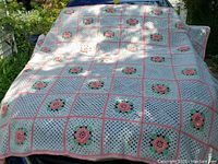 Full view of the crocheted bedspread draped over a surface showing the pattern of raised pink roses on square panels with pink and white crochet borders.