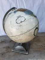 Front view of globe showing continents, oceans, and decorative title cartouche with metal square base