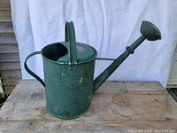 Front side view of the green metal watering can showing the large spout and top handle.