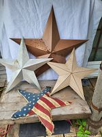 Photo showing the four stars with one large rust-colored metal star, two medium-sized off-white and beige metal stars, and one fabric star featuring an American flag design.