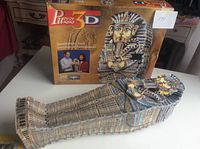 Completed 3D puzzle of King Tut sarcophagus displayed alongside its original box, showcasing the packaging and detailed artwork on the puzzle.
