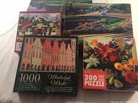 Five adult puzzles stacked, showing 'Wonderful World' 1000-piece, floral 300-piece, and garden house 300-piece puzzles.