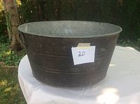 Full view of the round metal wash tub showing dark exterior color and size proportion on white table outdoors.