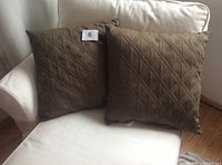 Two brown square cushions 18x18 inches on a white armchair. Both cushions feature a diamond quilted pattern on the fabric surface.