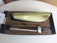 Electric knife placed on wooden and black plastic-lined storage holder with one blade attached.