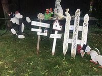 Overall view of numerous garden signs and decorative stakes in grass, including lettering and themed wooden and metal pieces.