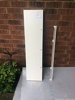 White rectangular floating shelf shown vertically upright next to metal mounting bracket against brick wall.