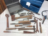 Blue and gray metal tool boxes beside assortment of old rusty hand tools on white surface