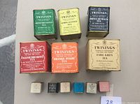 Top view of six larger metal tins and six smaller plastic tins, arranged in two rows showing label details and variety names of teas.