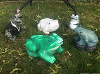Five vintage painted cement frog figurines arranged on grass outdoors in natural light.