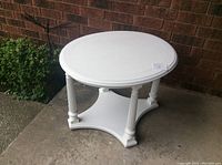 White oval wooden painted table showing top surface and legs, outdoors against brick wall.