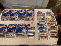 16 Hot Wheels cars in sealed original packaging laid out on table including 2002 series and 2017 Hot Rod series