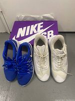 Two pairs of Nike tennis shoes, one white size 8.5 and one blue size 7, placed on a purple Nike SB box.