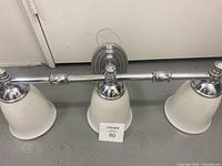Chrome finished bathroom vanity light fixture with three frosted glass shades mounted on a 24-inch wide bar, shown from left angle.
