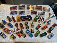 Overview photo showing 28 varied die cast cars and 9 Mustang collector cards spread on a white tablecloth.
