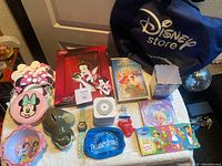 Photo showing all items on a table including Disney Store bag, Little Mermaid VHS, Frozen Blu-ray, Minnie Mouse pouches, Dumbo coin bank, watch, and character figures.