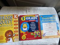 Three educational workbooks for young children including Brain Quest Kindergarten Workbook, Scholastic 1st Grade Workbook, and a Handwriting Practice Workbook.