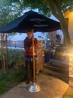 Photo of a person holding open a Fireball branded black patio umbrella with wooden pole and round metal base outside at dusk.