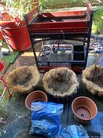 Vintage garden cart with several hanging plant holders and terra-cotta pots placed on ground with some other supplies.