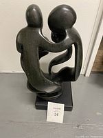Front view showing the abstract figures and their connected arms in a flowing design on a black base.