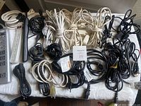 Top-down view of 23 power cables and extension cords in black and white, some coiled, on a white surface. Power strip visible on left.