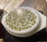 Top view of Pyrex casserole dish lid showing yellow-green olive branch pattern on white glass.