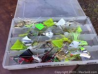 Photo showing one plastic tackle box open filled with buzz fishing spinnerbaits with metal blades and colorful skirted hooks, including chartreuse, white and black skirts.