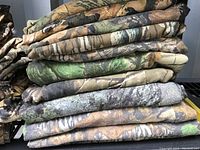 Stack of folded camouflage clothing showing various patterns and colors, mainly earth tones and green-based camo.